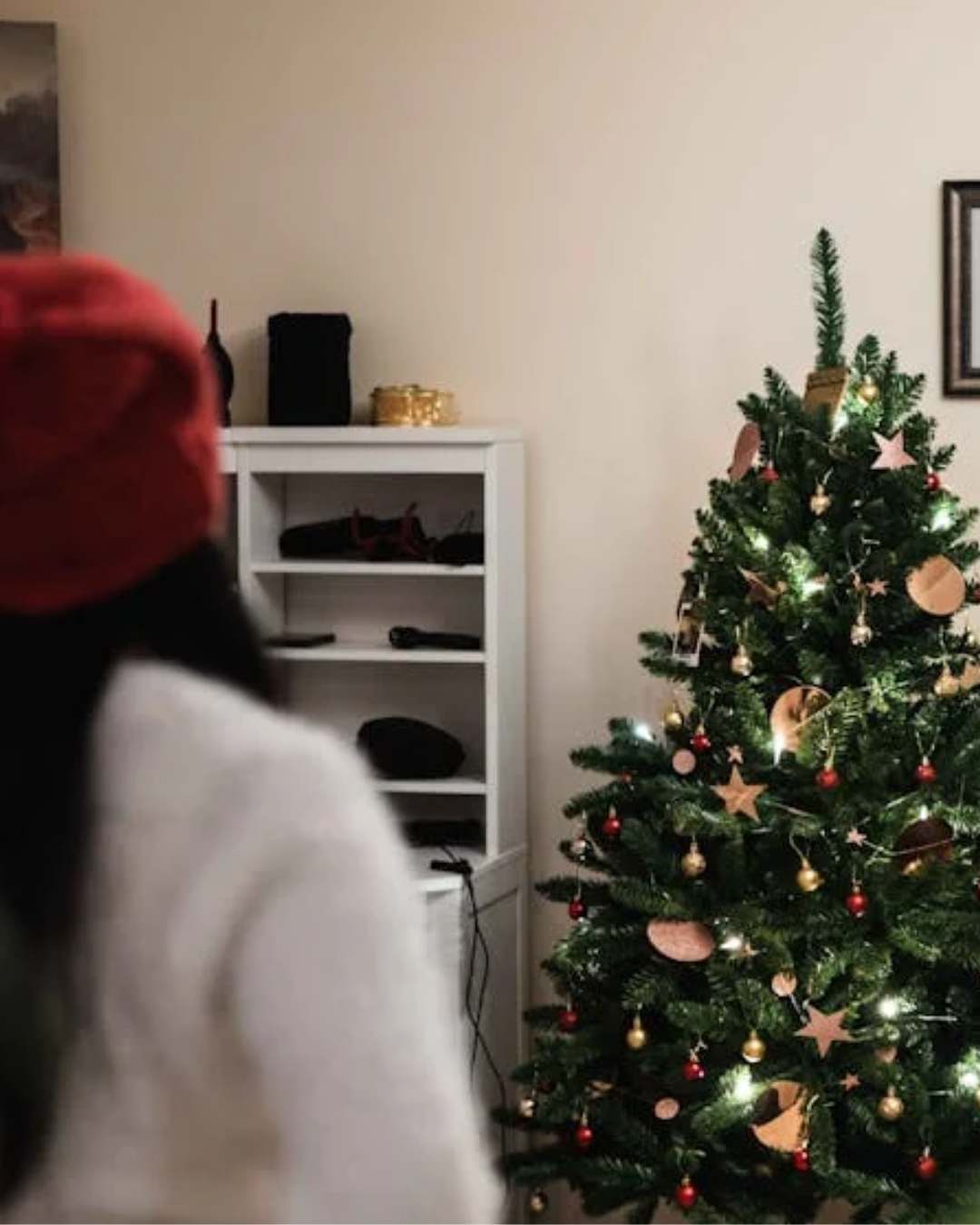 A person in a white sweater looking at a christmas tree